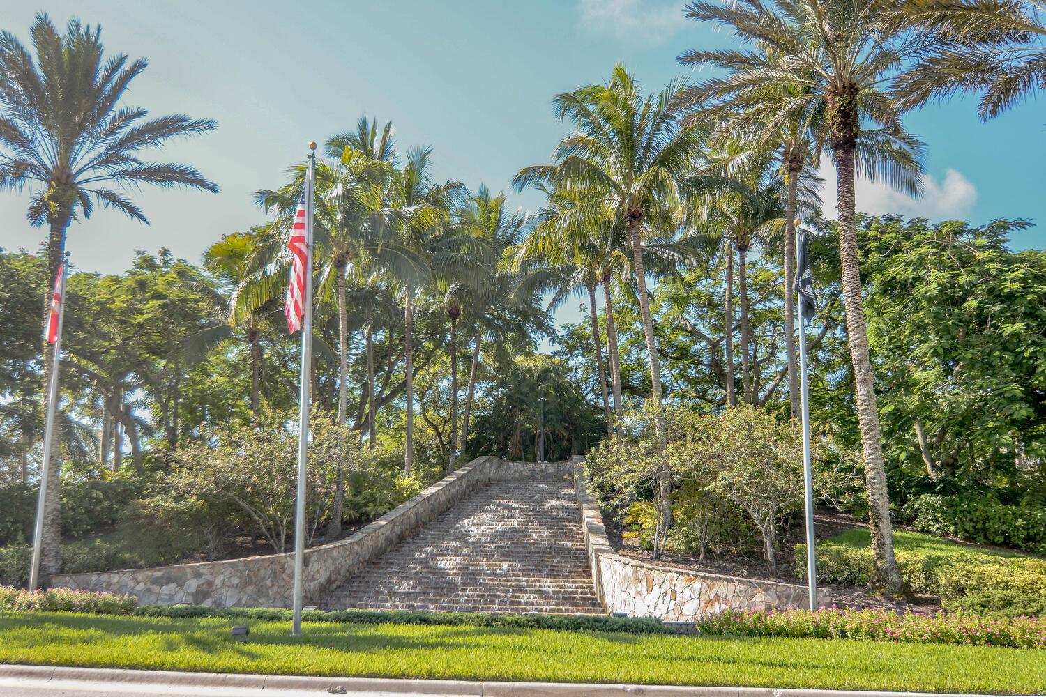A stone staircase leads up a landscaped hill flanked by palm trees and flagpoles — 4676 Manderly Drive, Wellington FL 33449, WELLINGTON, FL