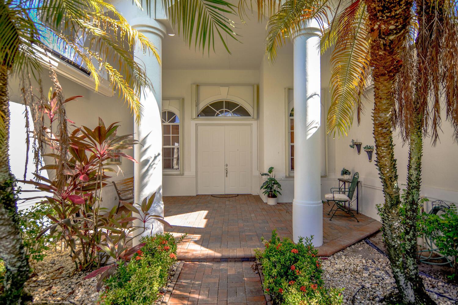 A covered brick entryway features white columns, double doors, and lush tropical landscaping — 4676 Manderly Drive, Wellington FL 33449, WELLINGTON, FL