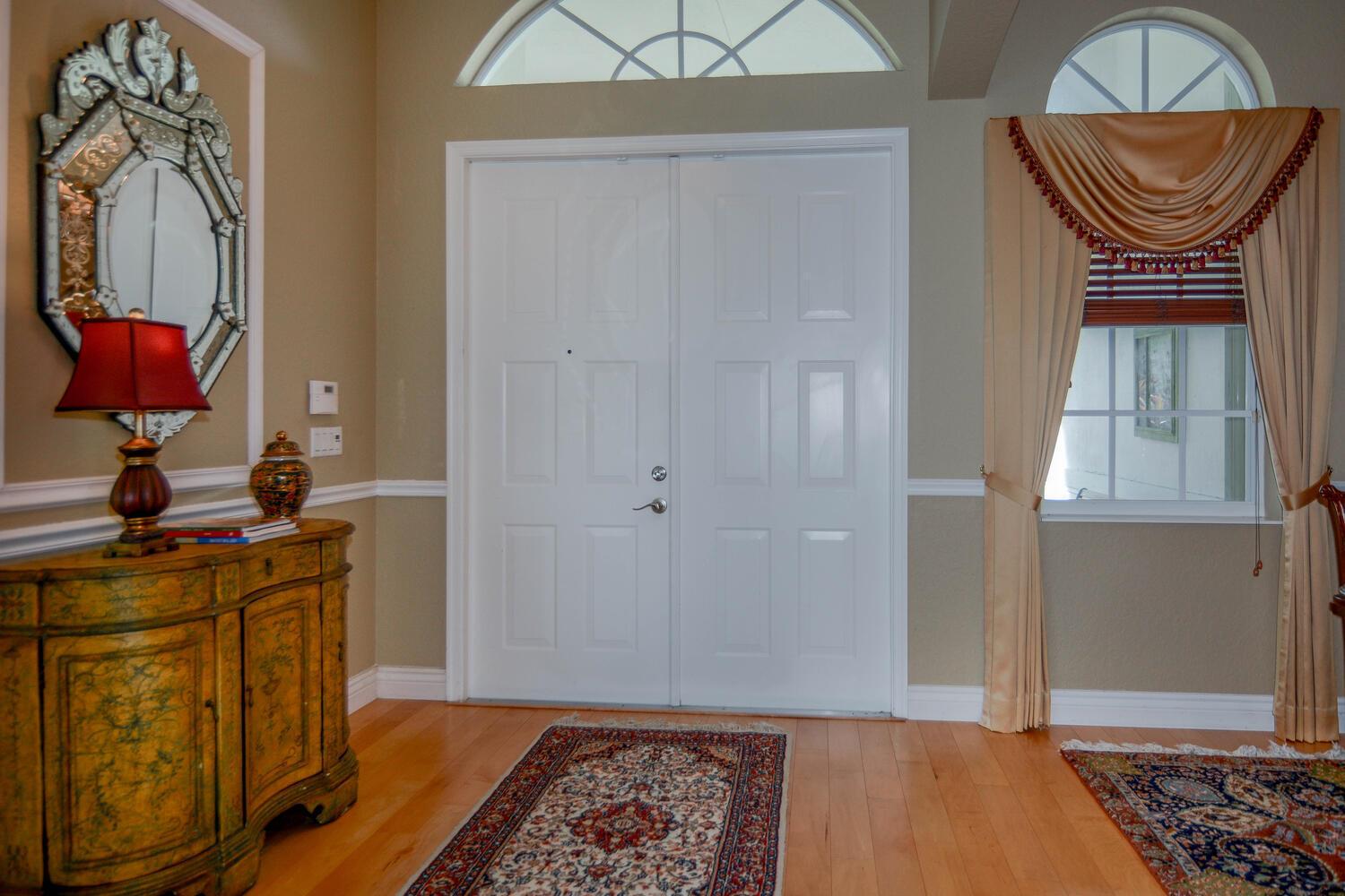 An entryway features double white doors, a decorative mirror, a wooden cabinet, and area rugs — 4676 Manderly Drive, Wellington FL 33449, WELLINGTON, FL