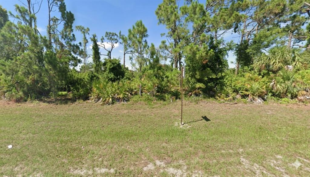 A vacant, grassy lot features dense trees and shrubs under a clear blue sky — 13364 KEYSTONE BOULEVARD, PORT CHARLOTTE, FL