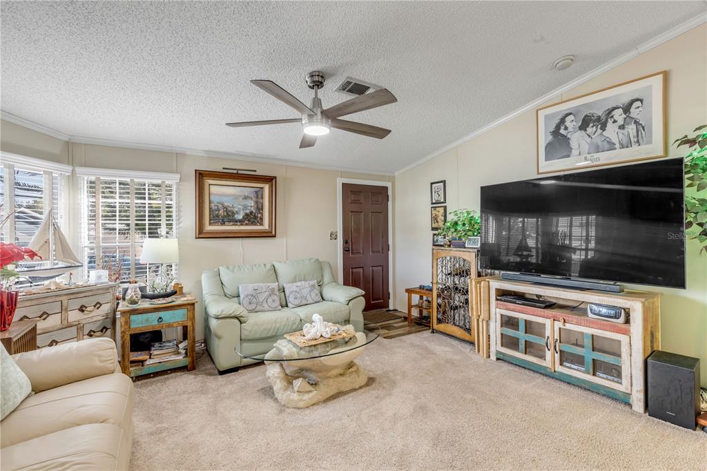 A living room features a light green loveseat, a large television, and a ceiling fan — 2201 S RIDGEWOOD AVENUE UNIT 28, EDGEWATER, FL
