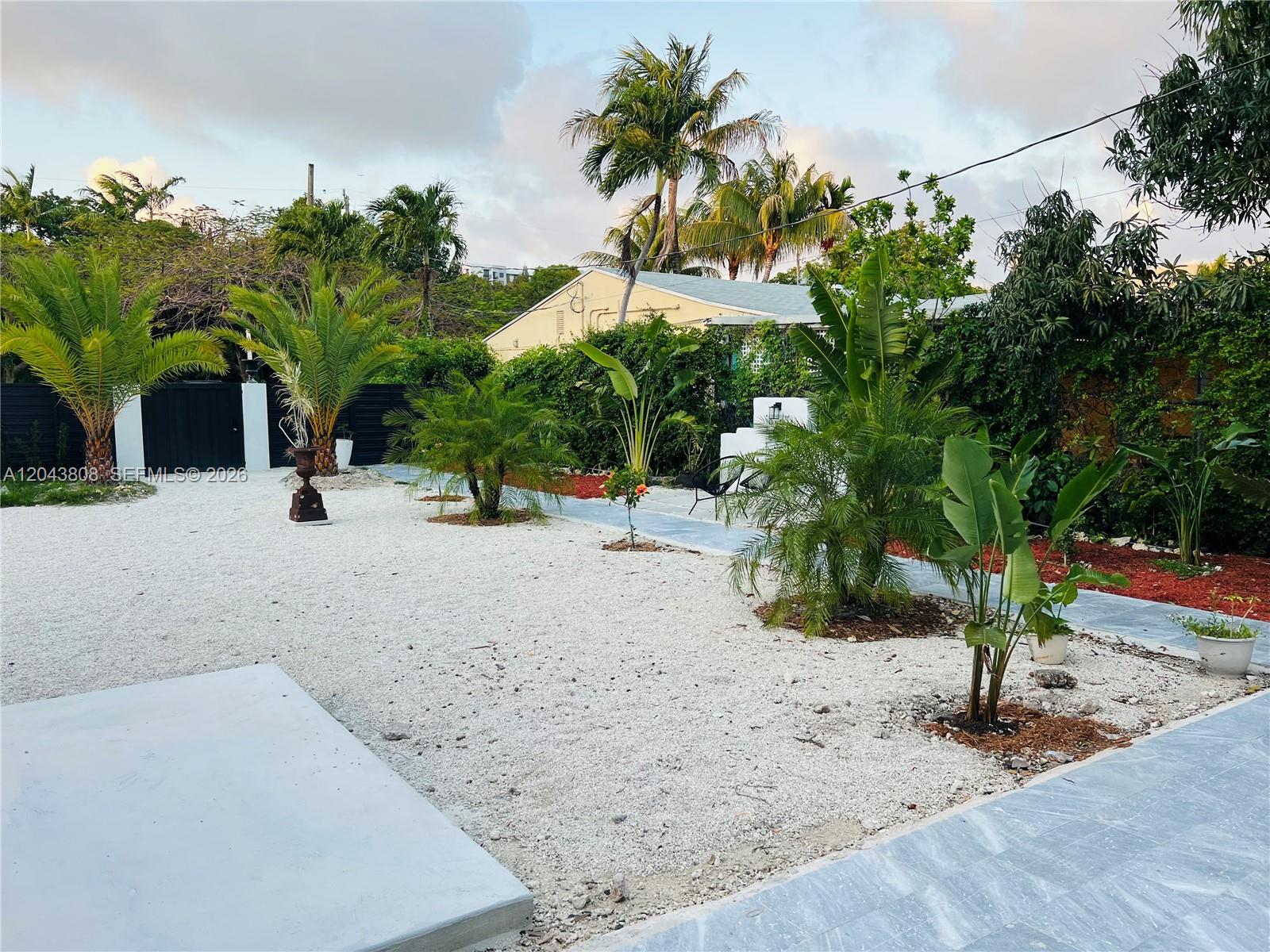 A landscaped backyard features white gravel, various palm trees, and gray stone walkways — 2134 SW 11th St, Miami FL 33135, MIAMI, FL