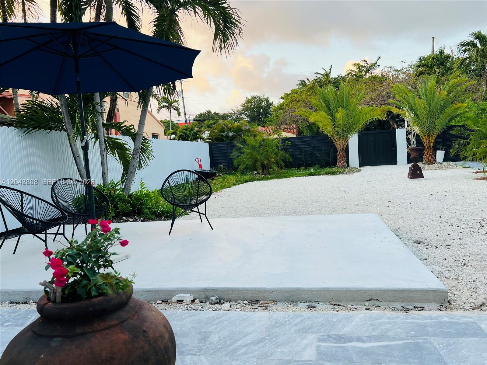 A patio features a concrete slab, black chairs, a blue umbrella, and gravel landscaping — 2134 SW 11th St, Miami FL 33135, MIAMI, FL