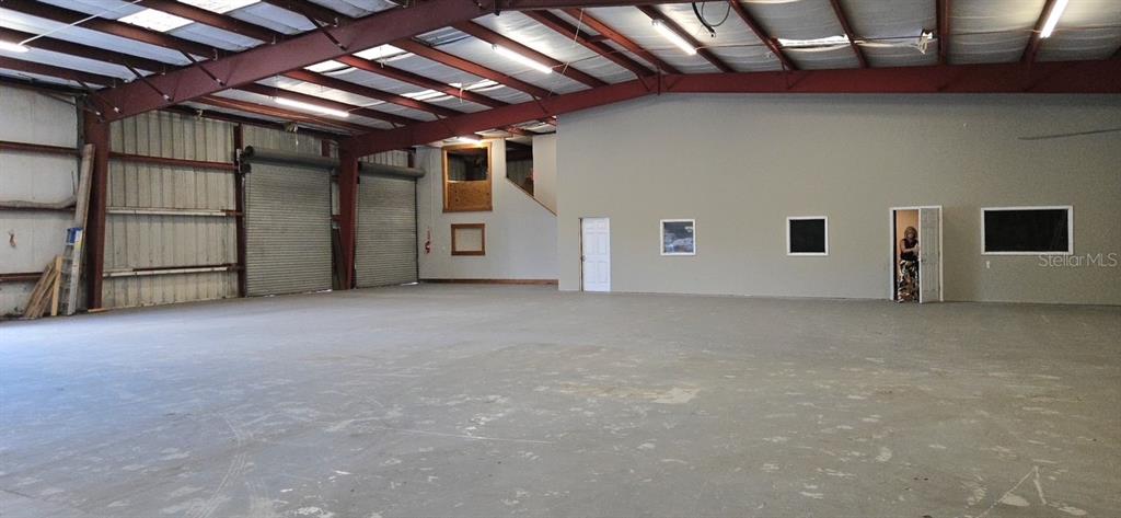 An expansive, open-concept warehouse interior features concrete floors, exposed steel beams, and roll-up doors — 9737 NEW YORK AVENUE, HUDSON, FL
