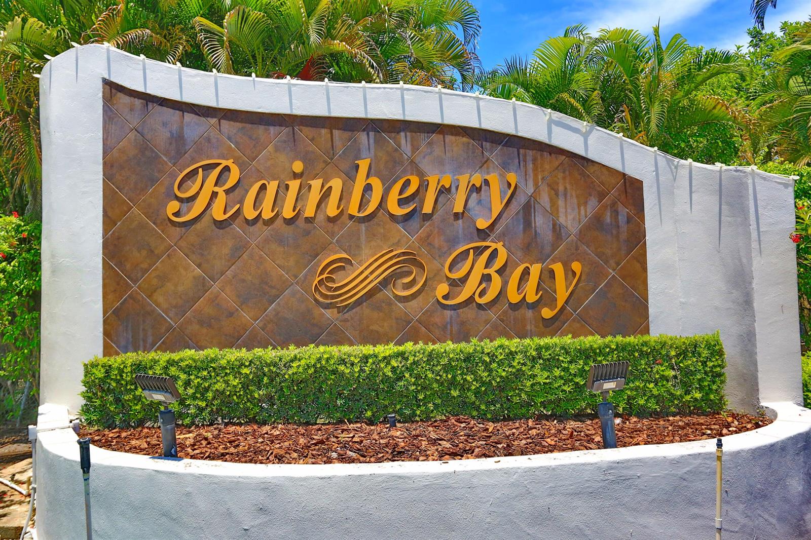 A sign for Rainberry Bay stands in front of a hedge and palm trees — 714 NW 27th Avenue # C, Delray Beach FL 33445, DELRAY BEACH, FL