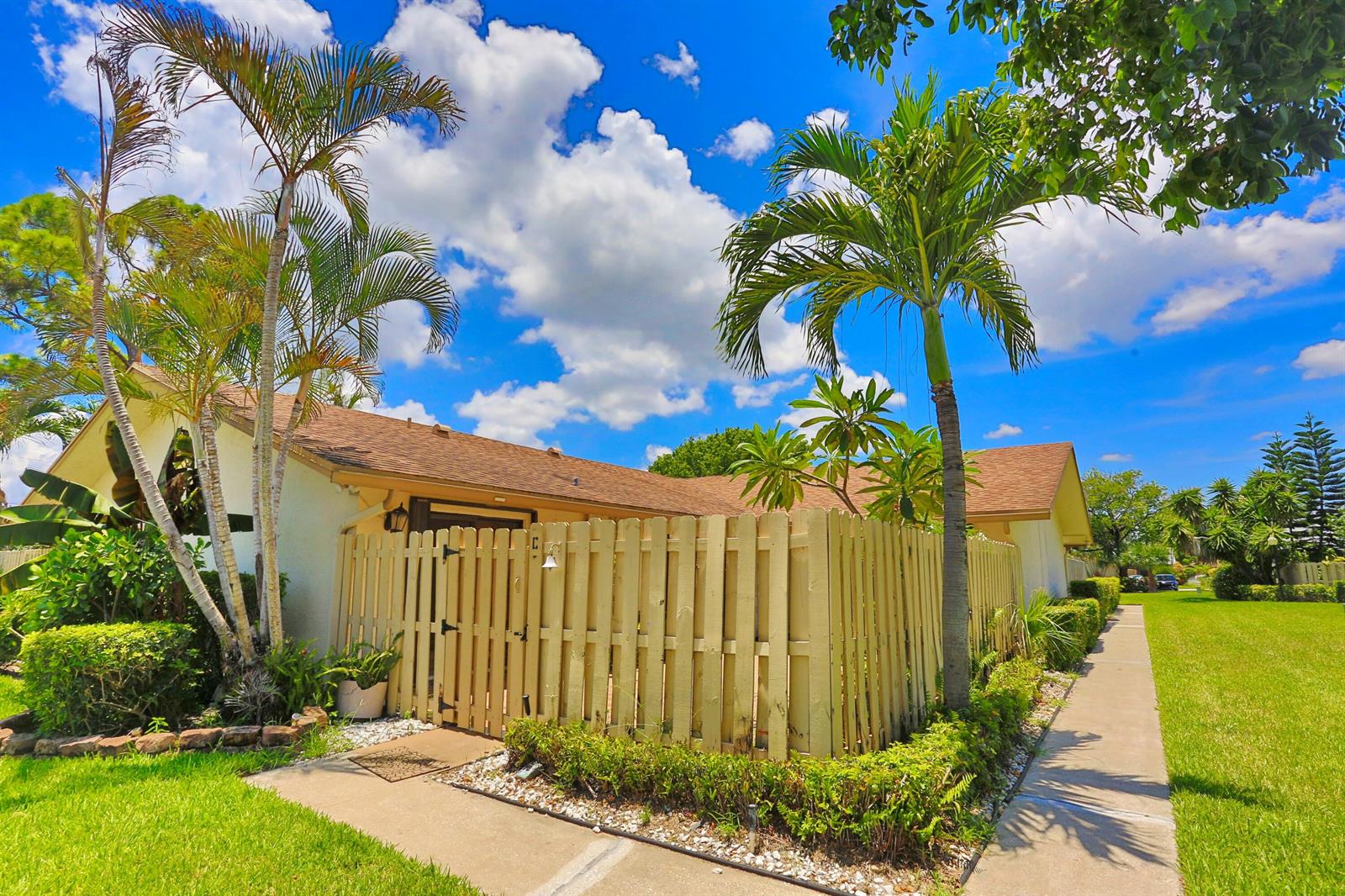 A view of a house exterior with a wooden fence, palm trees, and a sidewalk — 714 NW 27th Avenue # C, Delray Beach FL 33445, DELRAY BEACH, FL