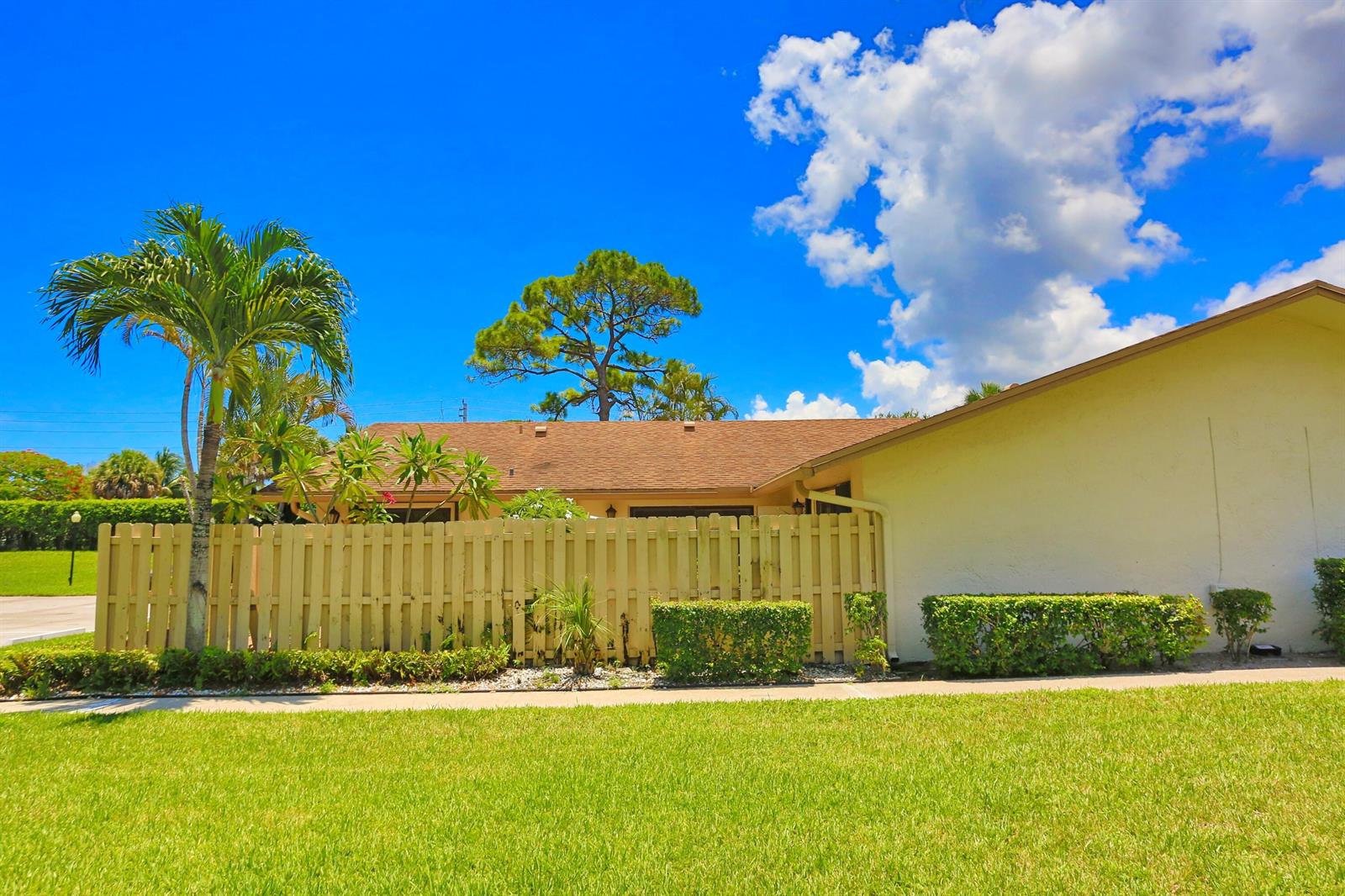 A light-colored house exterior features a wooden privacy fence, a palm tree, and green landscaping — 714 NW 27th Avenue # C, Delray Beach FL 33445, DELRAY BEACH, FL