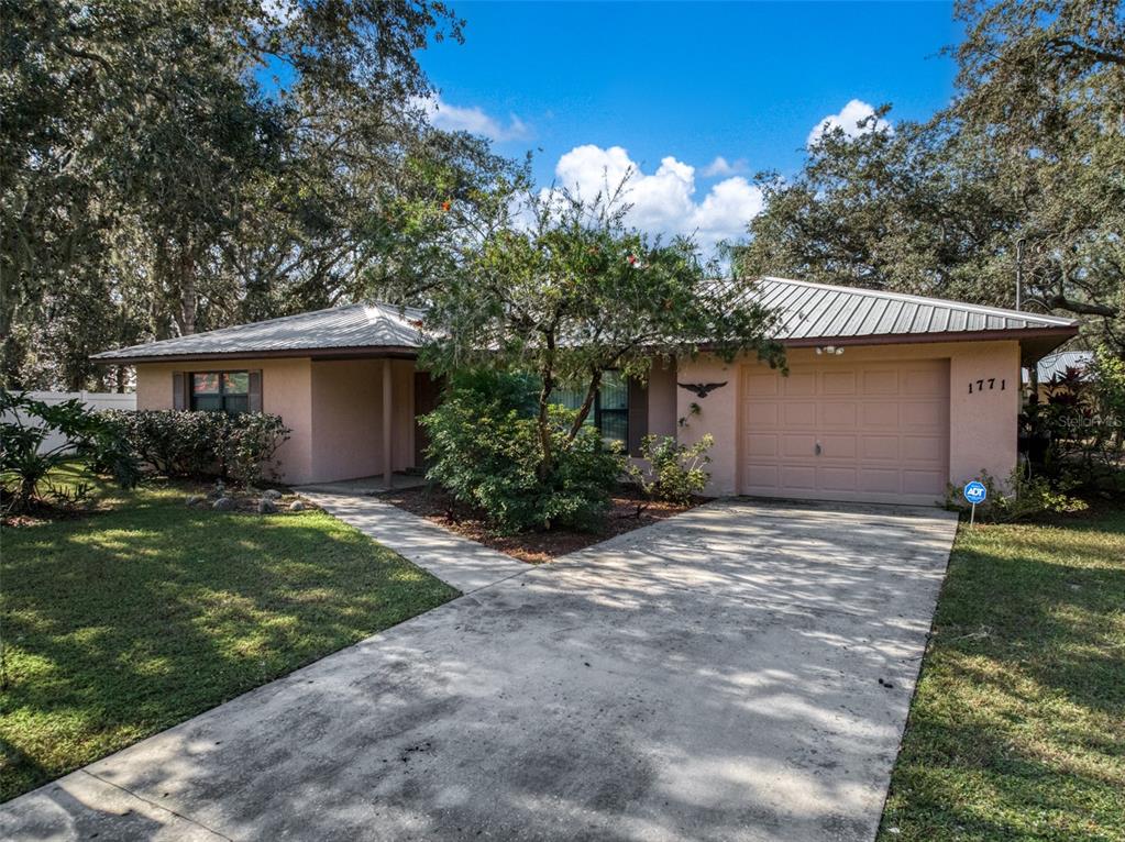 A single-story house with a metal roof, beige stucco exterior, and a concrete driveway — 1771 N TORRINGTON ROAD, AVON PARK, FL