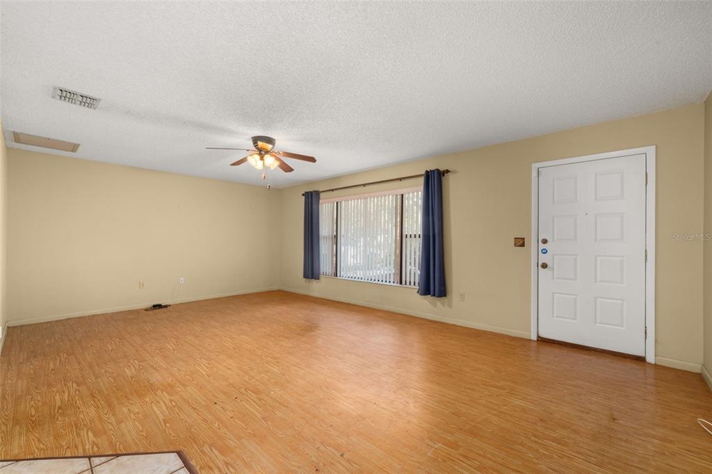 A living room with light wood-look flooring, beige walls, a ceiling fan, and a front door — 1771 N TORRINGTON ROAD, AVON PARK, FL