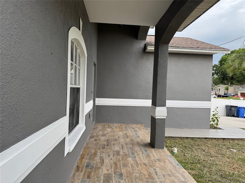 A covered porch features dark gray stucco walls, white trim, and wood-look tile flooring — 7202 N GLEN AVENUE, TAMPA, FL