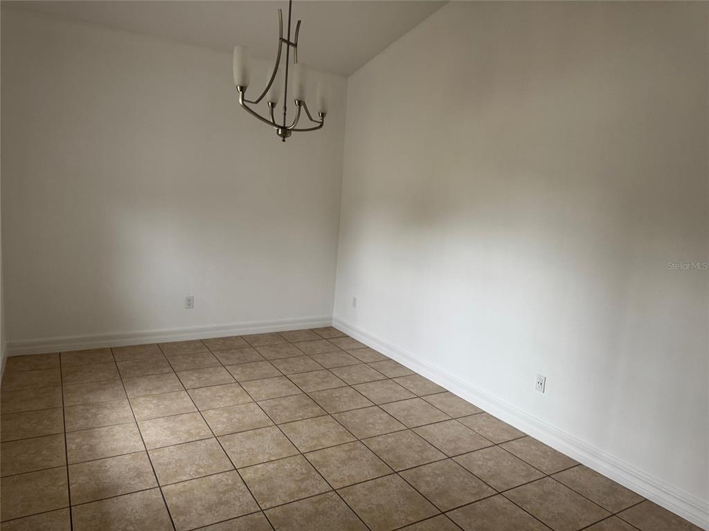 An empty dining room features white walls, a modern chandelier, and light brown tile flooring — 7202 N GLEN AVENUE, TAMPA, FL