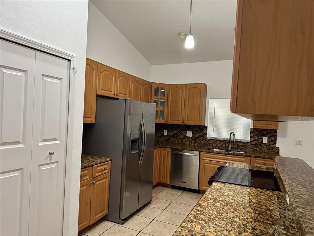 A kitchen features wood cabinets, granite countertops, stainless steel appliances, and tile flooring — 7202 N GLEN AVENUE, TAMPA, FL