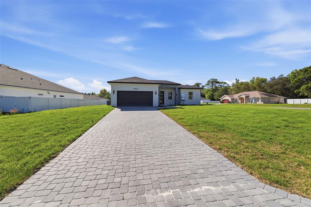 A single-story house with a paved driveway and a large front lawn under a blue sky — 12804 SW 74TH TERRACE, OCALA, FL
