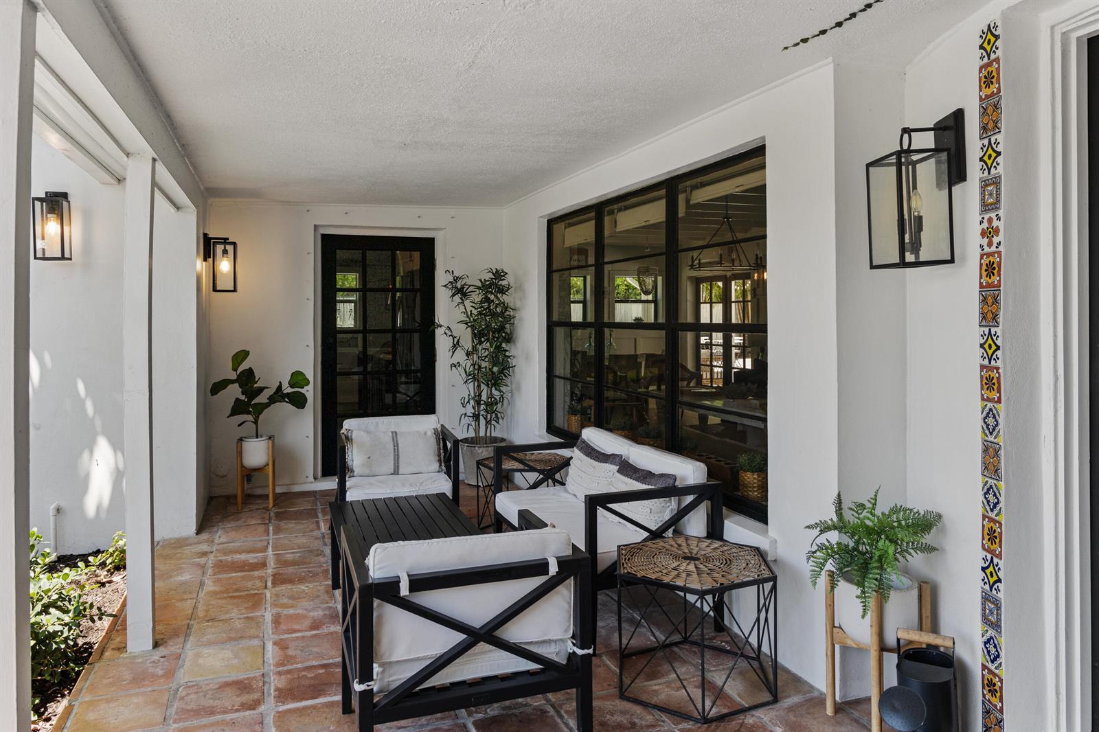 A covered patio features terracotta tile flooring, black-framed furniture, and decorative vertical tile accents — 711 SW 27th Way, Boynton Beach FL 33435, BOYNTON BEACH, FL
