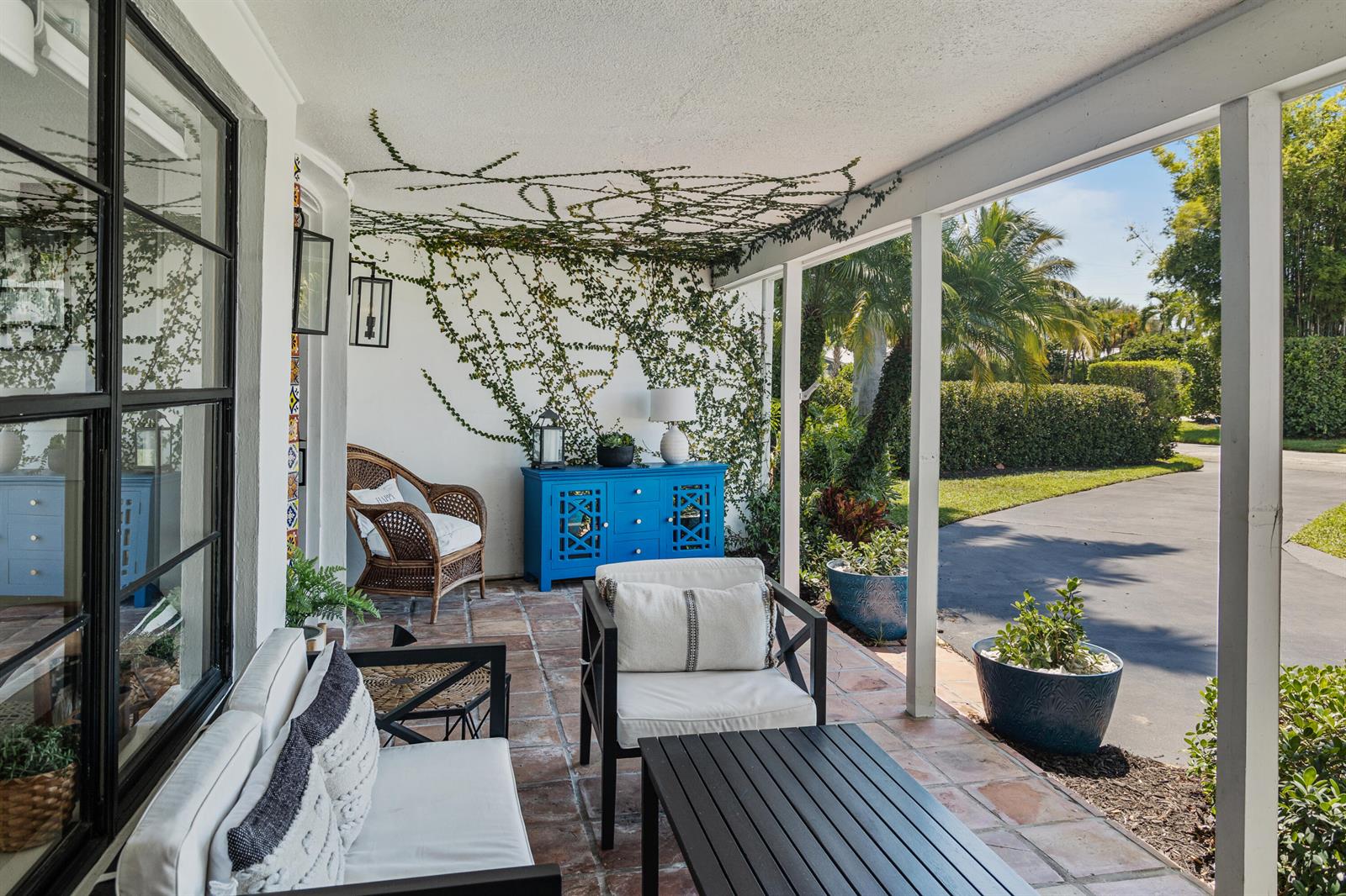 A covered patio features terracotta tile flooring, white walls with climbing vines, and outdoor furniture — 711 SW 27th Way, Boynton Beach FL 33435, BOYNTON BEACH, FL