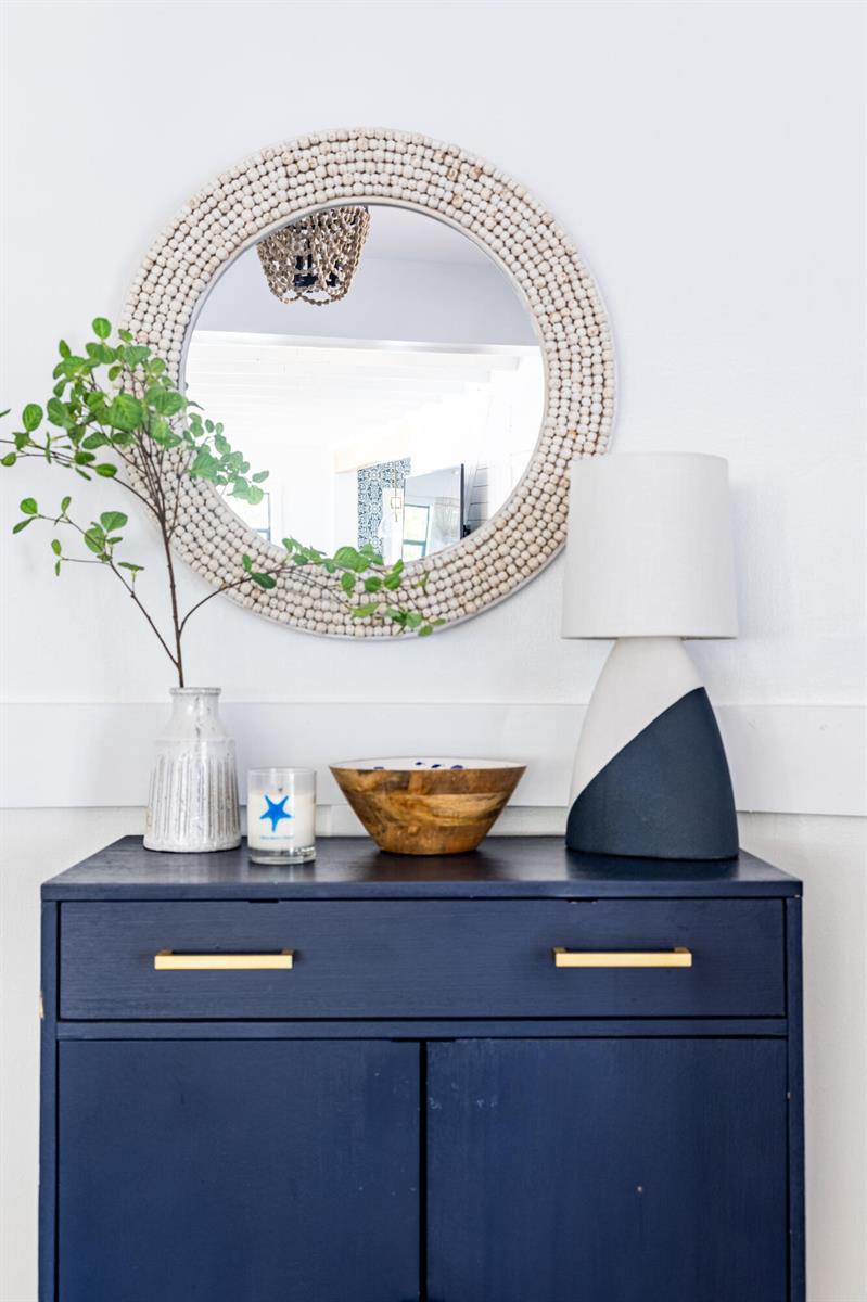 A navy blue cabinet sits below a round beaded mirror and a modern table lamp — 711 SW 27th Way, Boynton Beach FL 33435, BOYNTON BEACH, FL