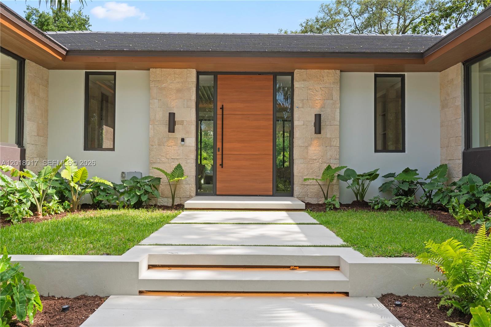 A modern home entrance features a wood door, stone facade, and a concrete walkway — 7840 SW 98th St, Miami FL 33156, MIAMI, FL