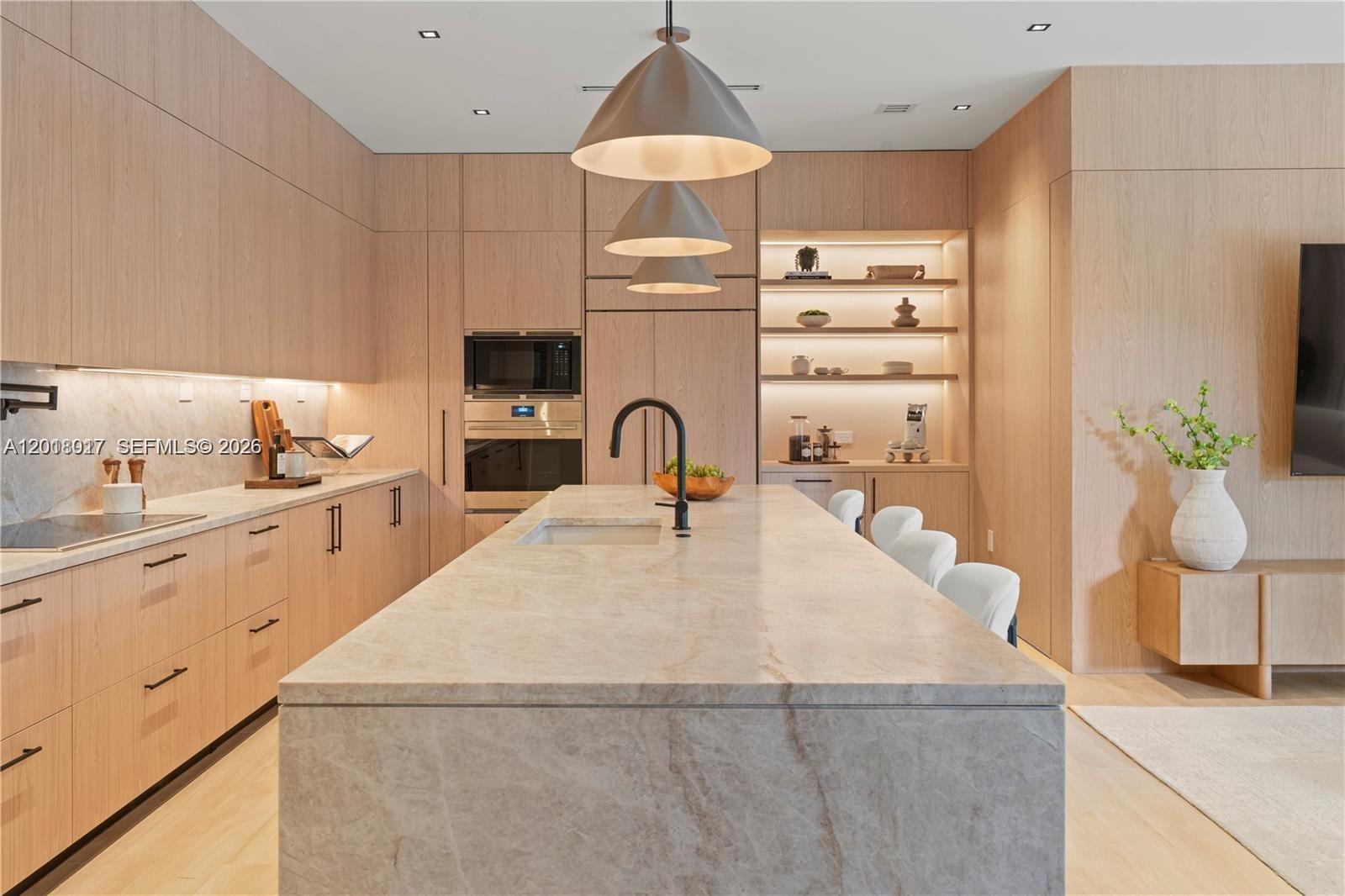 A modern kitchen features light wood cabinetry, a large stone island, and integrated appliances — 7840 SW 98th St, Miami FL 33156, MIAMI, FL