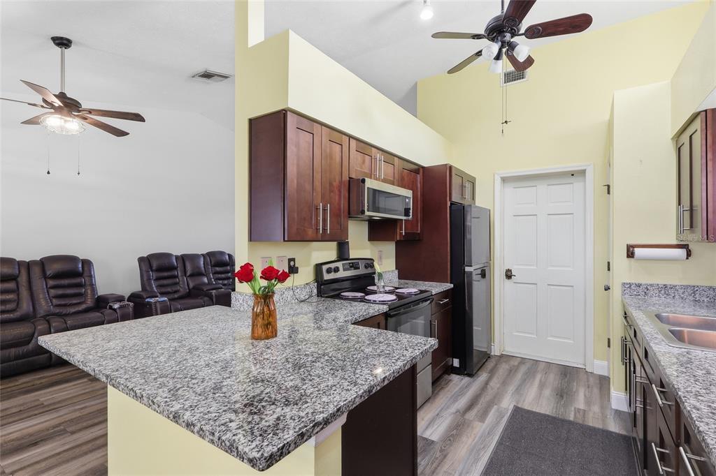 A kitchen with granite countertops and dark wood cabinets opens into a living area — 1405 E FRANCES AVENUE, PLANT CITY, FL