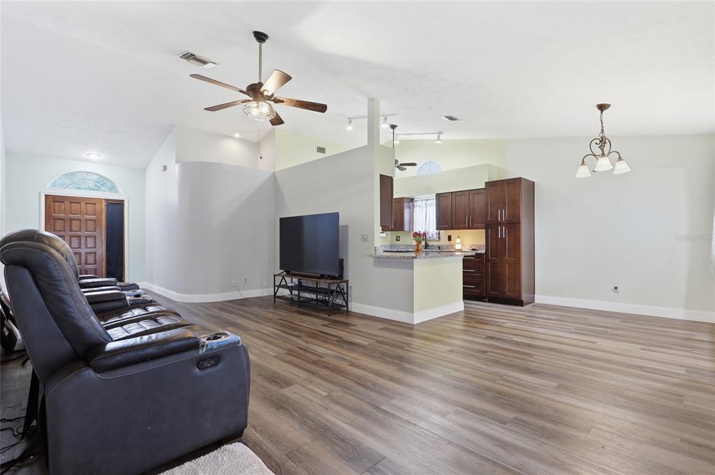 A living room with wood-look flooring, a ceiling fan, and an open kitchen with dark cabinets — 1405 E FRANCES AVENUE, PLANT CITY, FL