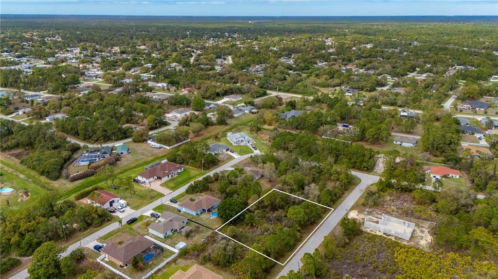 An aerial view shows a vacant, wooded residential lot outlined in white within a neighborhood — PAIGO LANE, NORTH PORT, FL