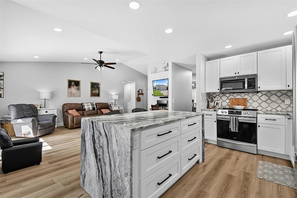 A kitchen with a large marble-topped island and white cabinets opens into a living room — 1 ROUND TREE DRIVE, PALM COAST, FL