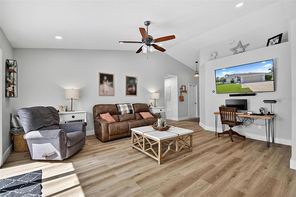 A living room features wood-look flooring, a brown sofa, a gray recliner, and a wall-mounted television — 1 ROUND TREE DRIVE, PALM COAST, FL