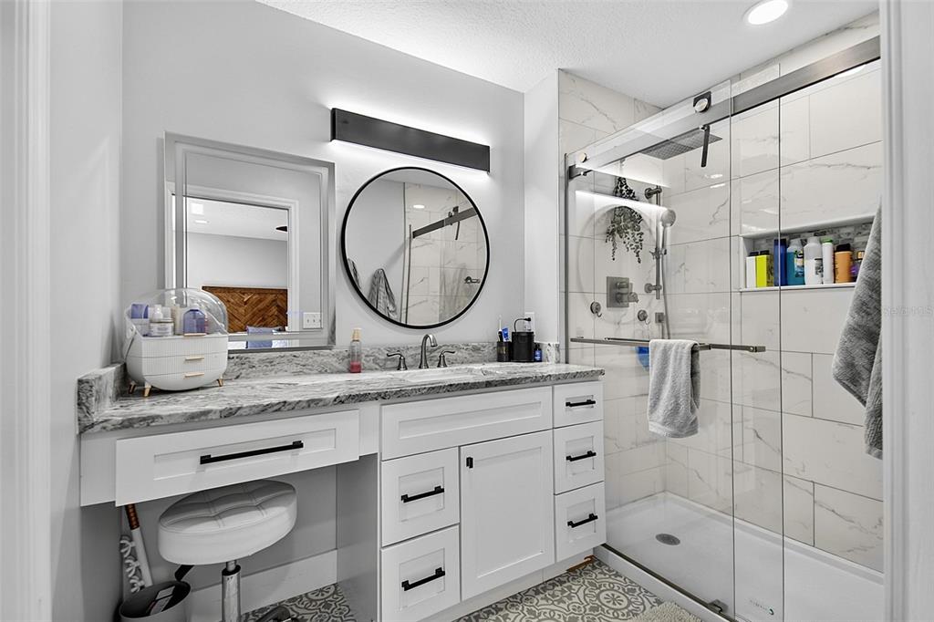 A bathroom features a white vanity with a marble countertop, a round mirror, and a shower — 1 ROUND TREE DRIVE, PALM COAST, FL