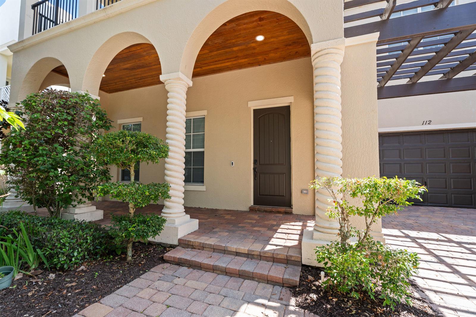 A tan house exterior features a covered porch with spiral columns and a wooden ceiling — 112 Tulip Tree Court, Jupiter FL 33458, JUPITER, FL