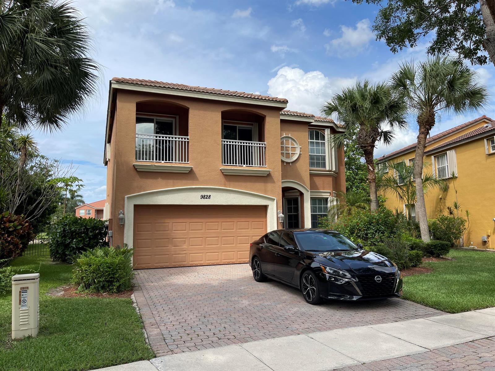 A two-story tan stucco house with a two-car garage and a black sedan parked outside — 9828 Stover Way, Wellington FL 33414, WELLINGTON, FL