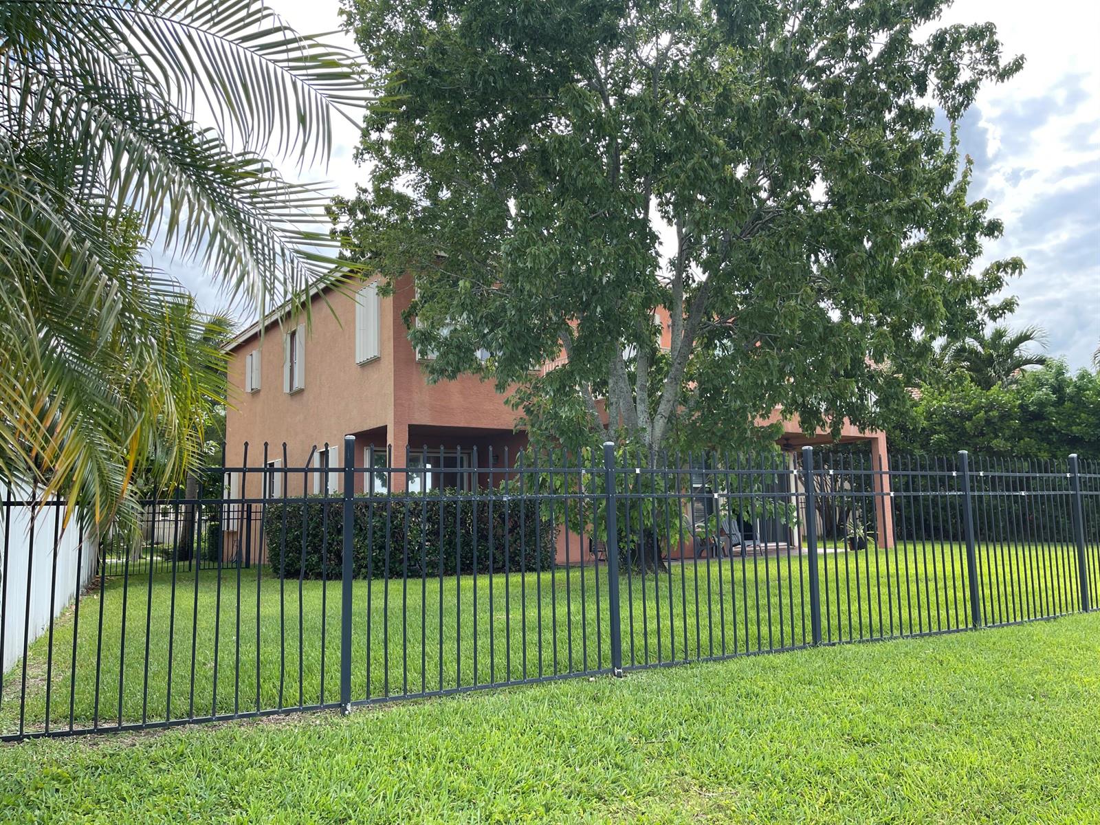 A two-story peach-colored house sits behind a black metal fence in a grassy yard — 9828 Stover Way, Wellington FL 33414, WELLINGTON, FL