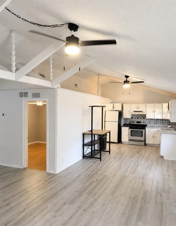 An open-concept kitchen and living area features white cabinets, light wood flooring, and vaulted ceilings — 1505 N ORANGE STREET, PLANT CITY, FL