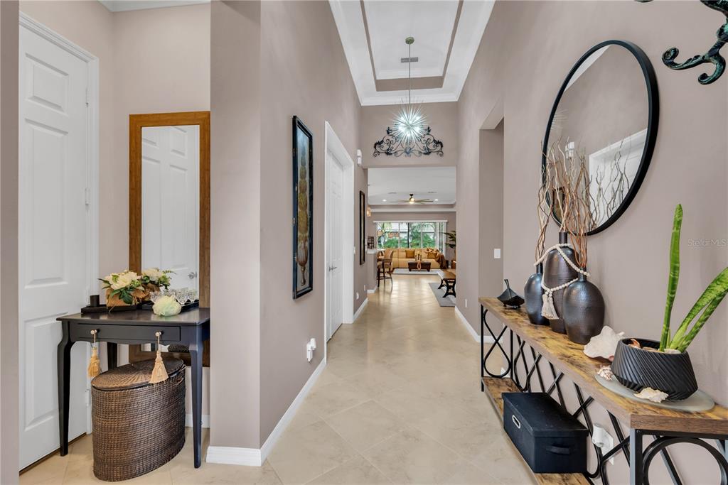 A bright foyer features tile flooring, a console table, a round mirror, and a hallway view — 4853 GRAND BANKS DRIVE, WIMAUMA, FL