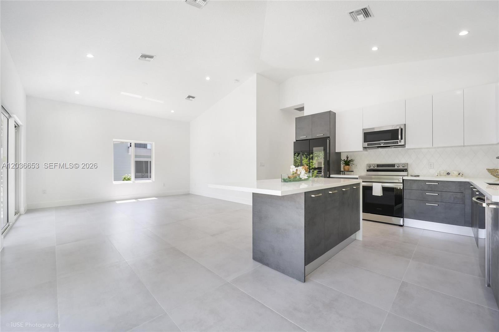 A modern kitchen with dark grey cabinets and a white island opens to a living area — 5 Bowen Dr, Key Largo FL 33037, KEY LARGO, FL