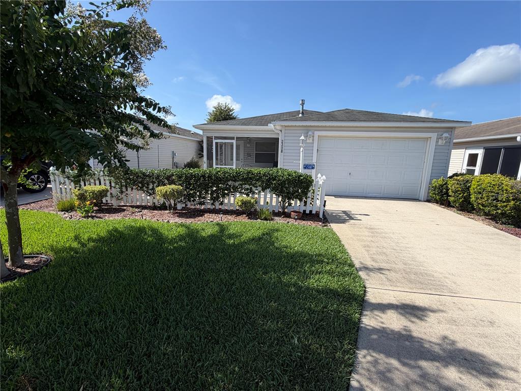 A single-story house features a white picket fence, a concrete driveway, and a garage — 2318 OAK BEND PLACE, THE VILLAGES, FL