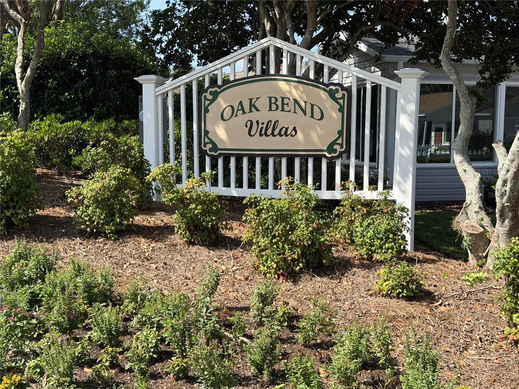 A white picket fence sign for Oak Bend Villas stands in a landscaped garden area — 2318 OAK BEND PLACE, THE VILLAGES, FL