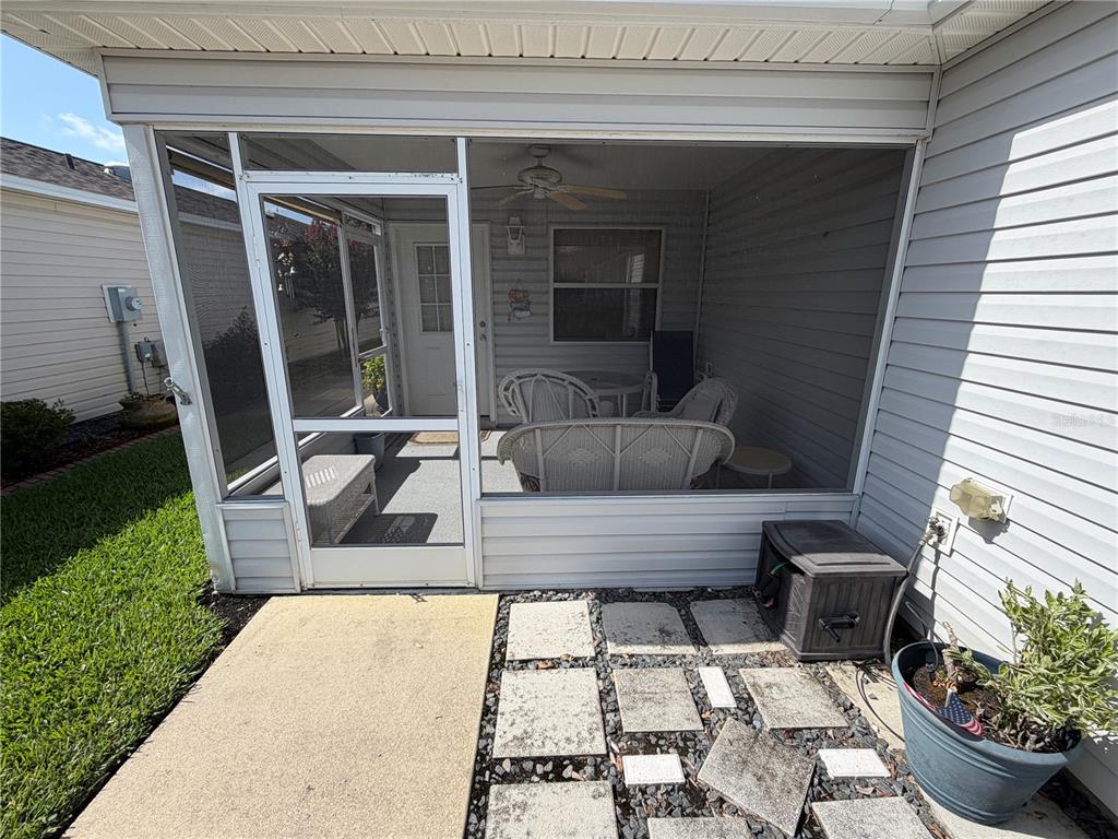 A screened-in porch with white wicker furniture sits beside a house with light-colored siding — 2318 OAK BEND PLACE, THE VILLAGES, FL