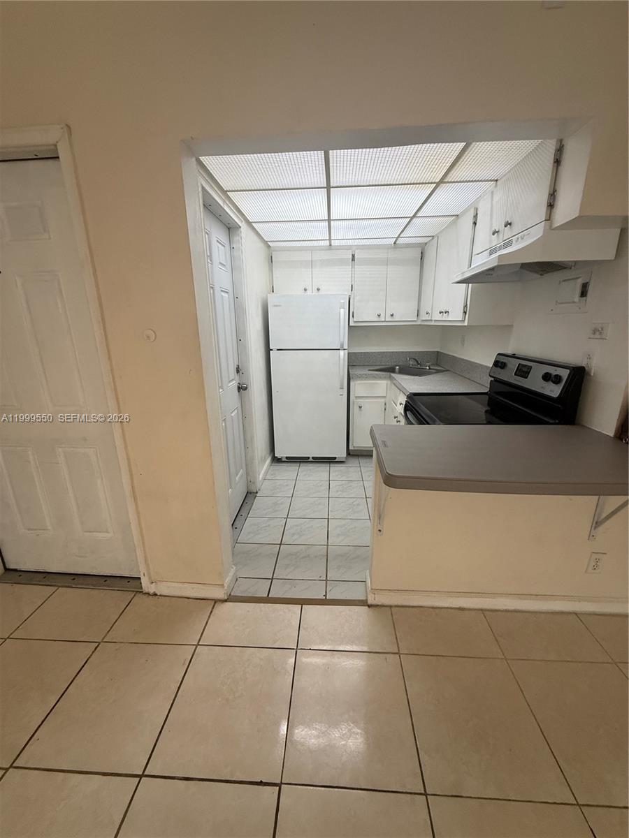 A galley-style kitchen features white cabinets, a white refrigerator, and light-colored tile flooring — 201 SE 6th Ave # 7, Pompano Beach FL 33060, POMPANO BEACH, FL