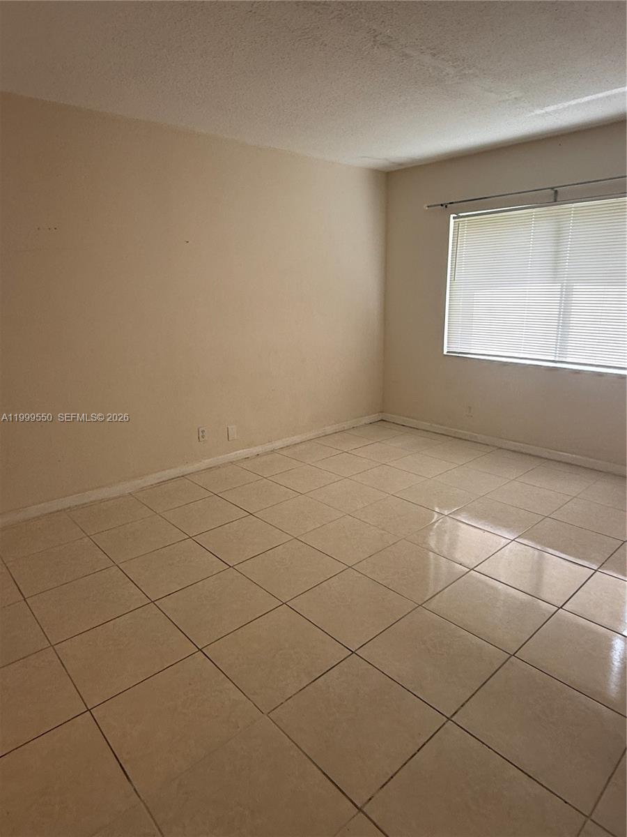 An empty room features beige walls, light-colored tile flooring, and a window with blinds — 201 SE 6th Ave # 7, Pompano Beach FL 33060, POMPANO BEACH, FL