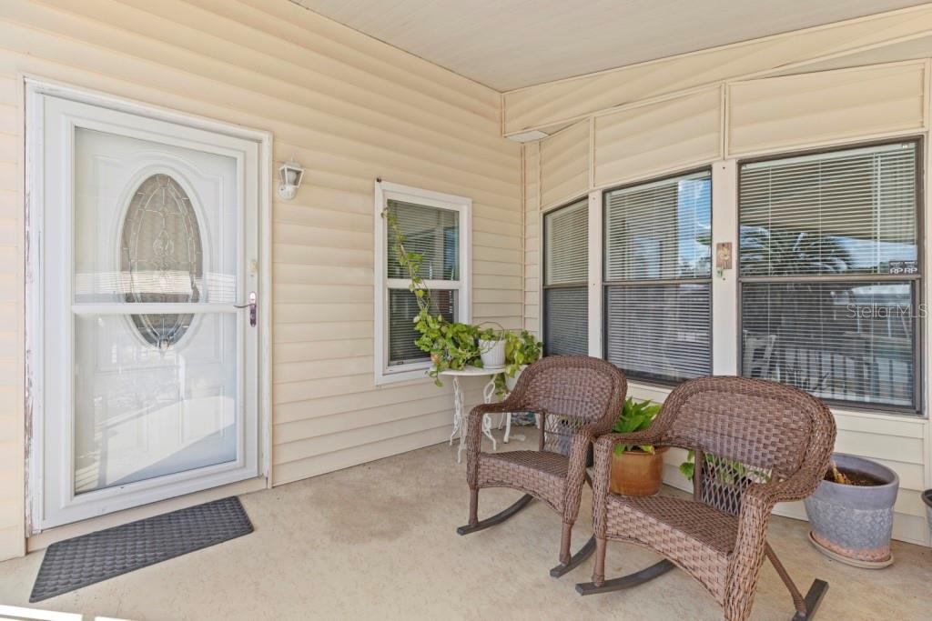 A covered porch features light-colored siding, a white front door, and two wicker rocking chairs — 35057 MCCULLOUGHS LEAP, ZEPHYRHILLS, FL