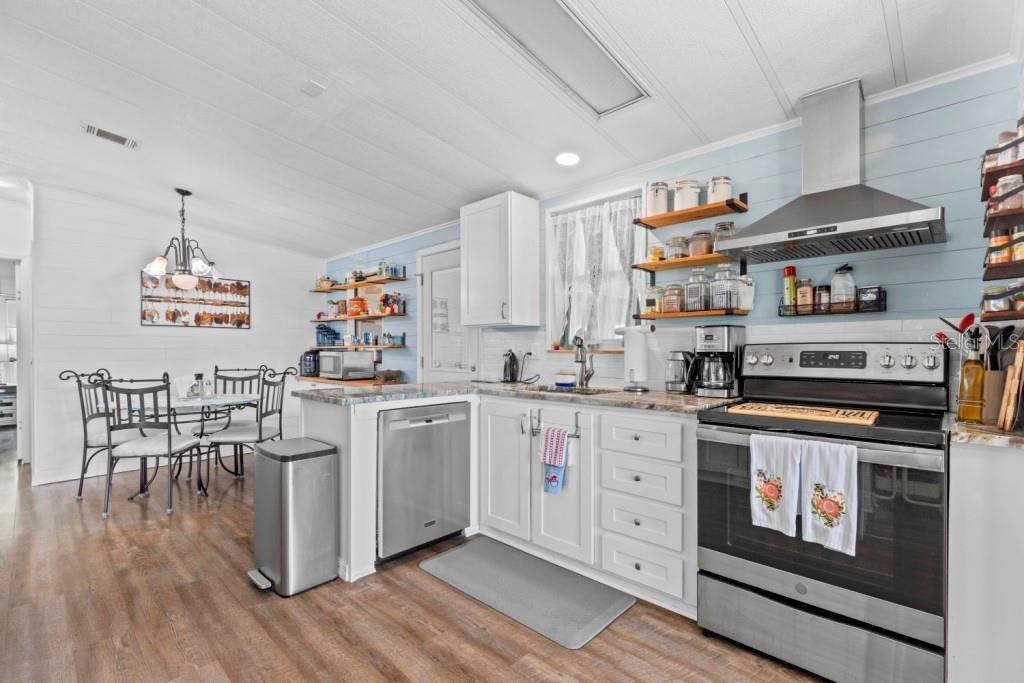 A kitchen with white cabinets, stainless steel appliances, open shelving, and an adjacent dining area — 35057 MCCULLOUGHS LEAP, ZEPHYRHILLS, FL