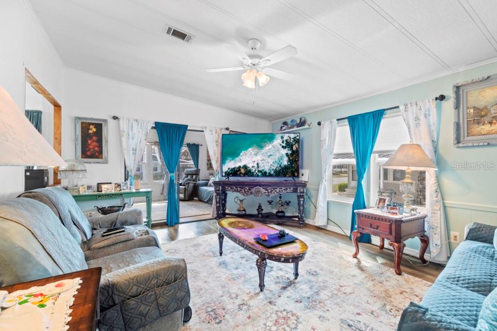 A living room features a television, a coffee table, two sofas, and blue curtains — 35057 MCCULLOUGHS LEAP, ZEPHYRHILLS, FL