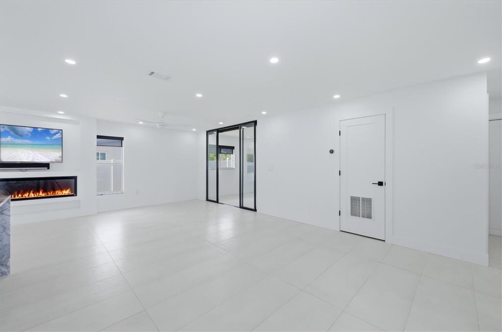 A bright, minimalist living room features white tile floors, a linear fireplace, and glass-paned doors — 201 HONORE AVENUE, SARASOTA, FL