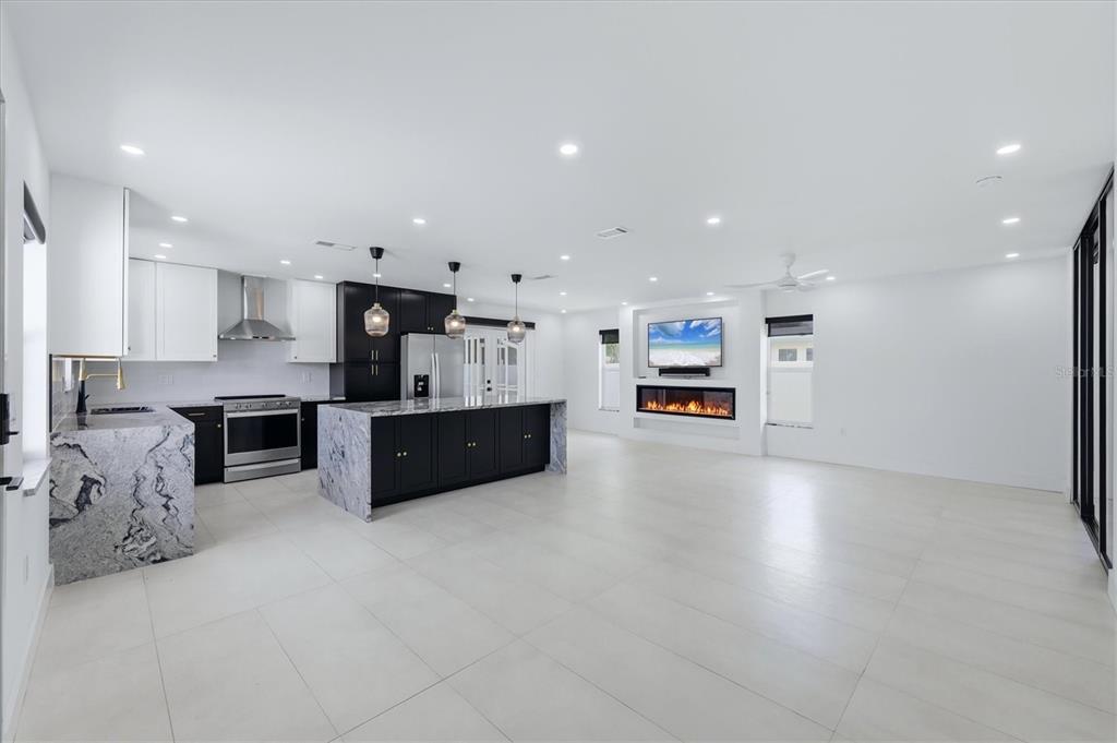 A modern open-concept kitchen and living area featuring black cabinetry, marble countertops, and a fireplace — 201 HONORE AVENUE, SARASOTA, FL