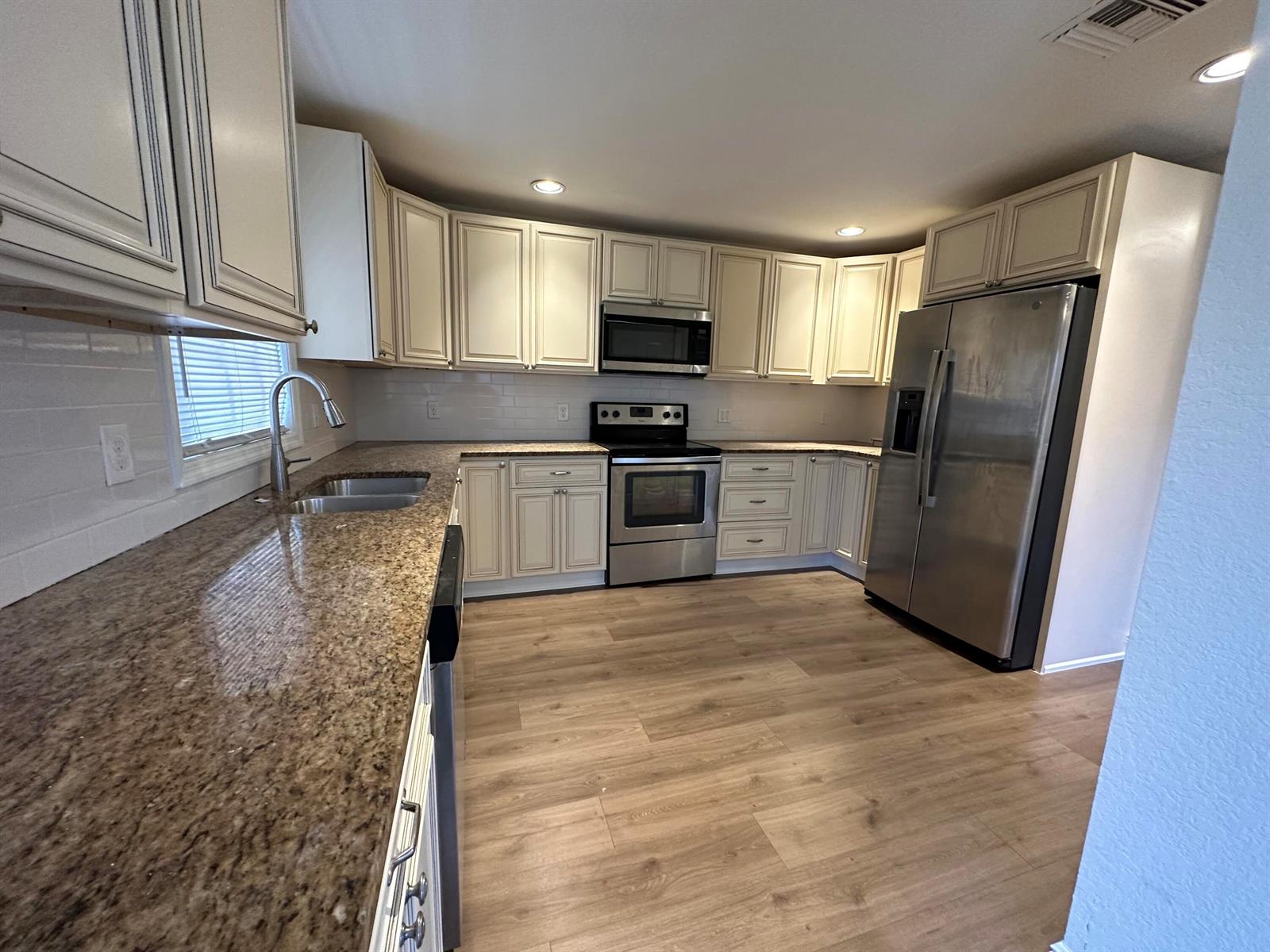 A kitchen features light-colored cabinets, granite countertops, stainless steel appliances, and wood-look flooring — 340 Walton Boulevard, West Palm Beach FL 33405, WEST PALM BEACH, FL