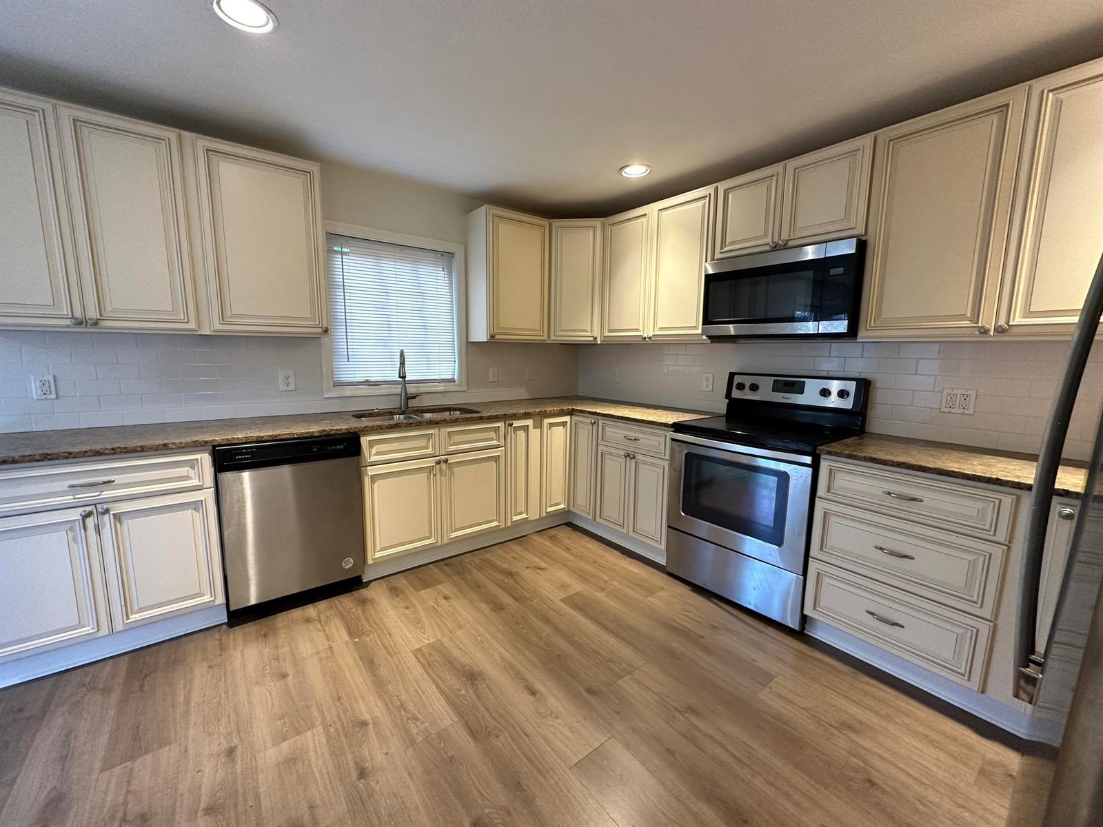 A kitchen features cream-colored cabinets, stainless steel appliances, granite countertops, and light wood flooring — 340 Walton Boulevard, West Palm Beach FL 33405, WEST PALM BEACH, FL