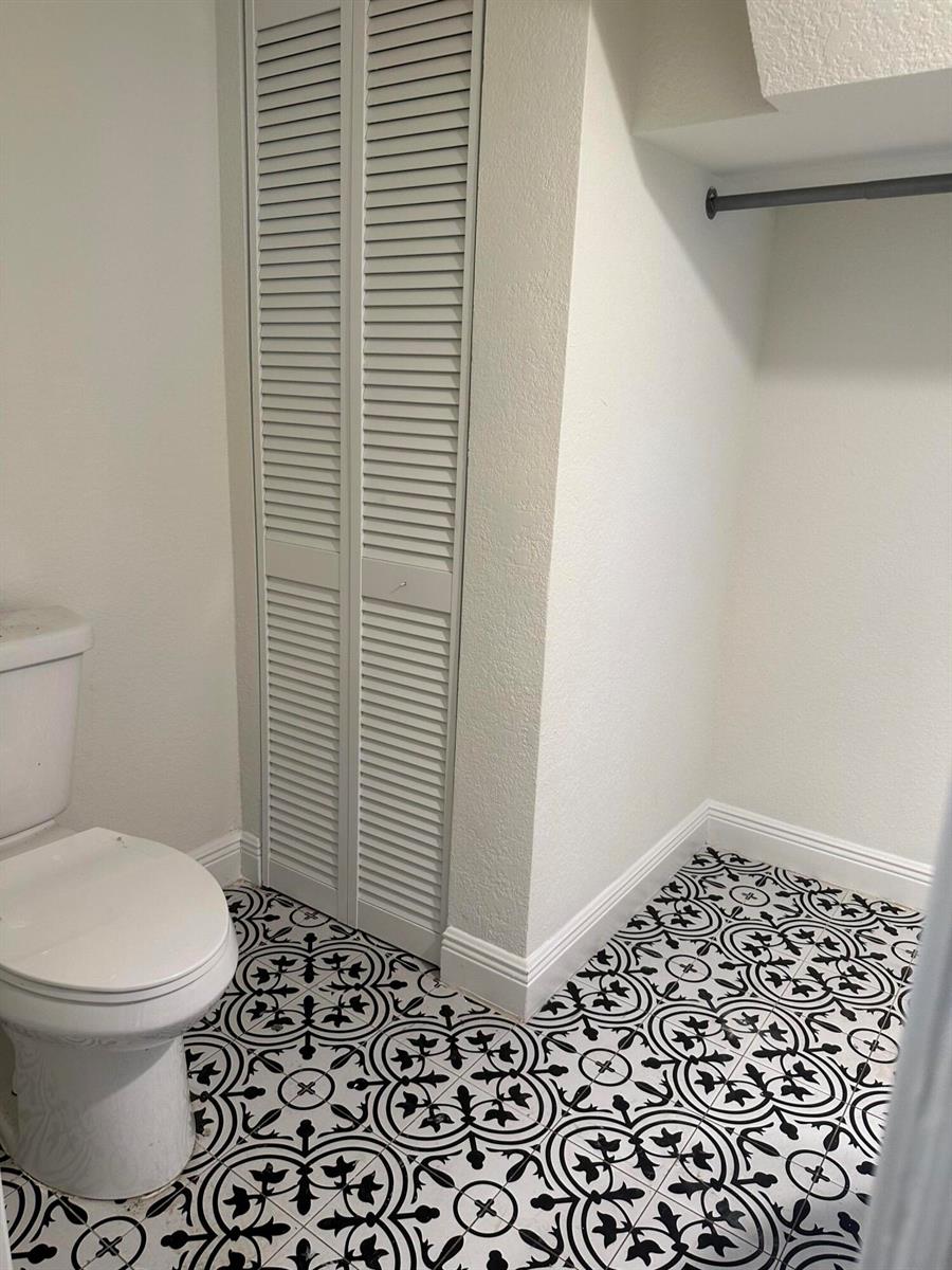 A bathroom features a toilet, louvered closet doors, and patterned black and white floor tiles — 340 Walton Boulevard, West Palm Beach FL 33405, WEST PALM BEACH, FL