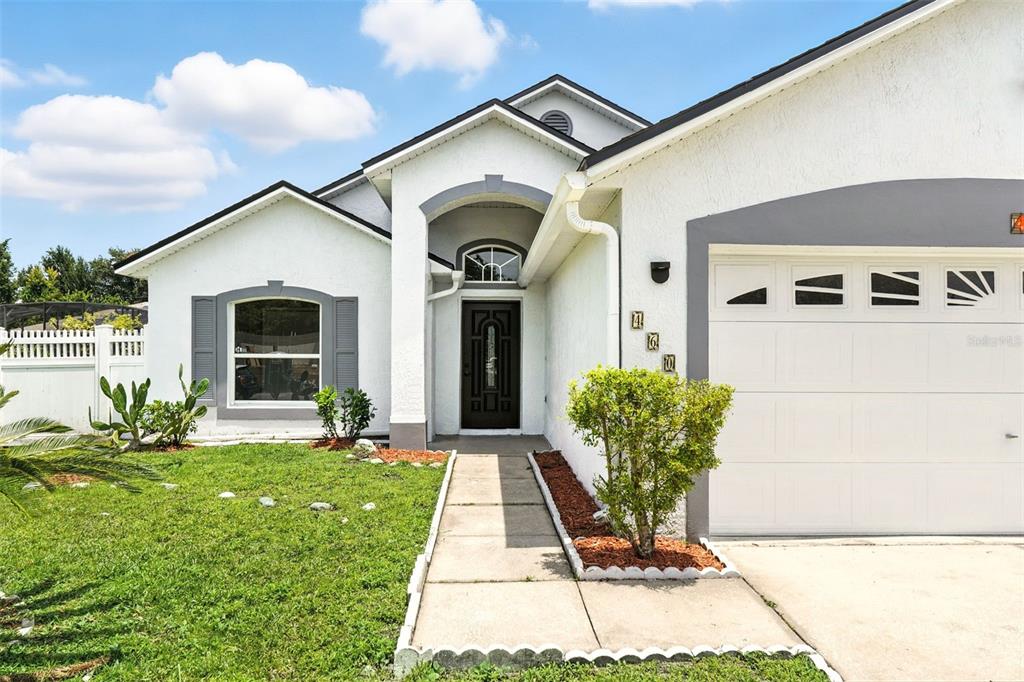 The exterior of a single-story home features a white stucco facade, gray trim, and a walkway — 460 MARTIGUES DRIVE, KISSIMMEE, FL