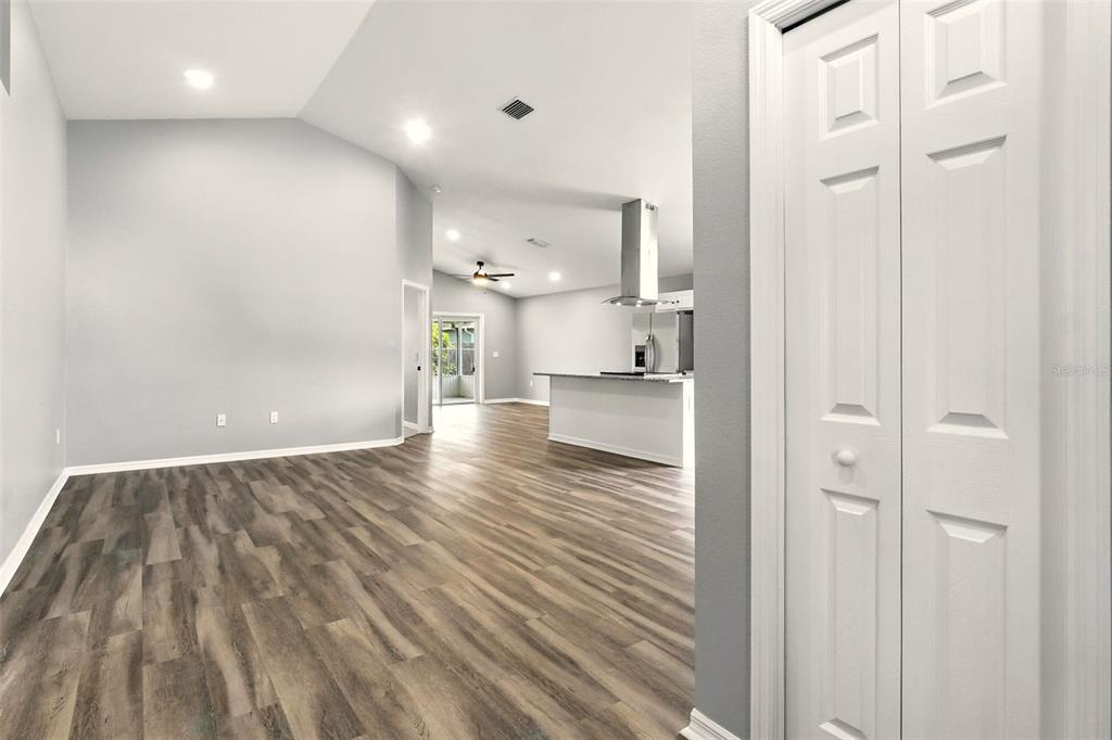 An open-concept living area with light gray walls, wood-look flooring, and a kitchen in back — 460 MARTIGUES DRIVE, KISSIMMEE, FL