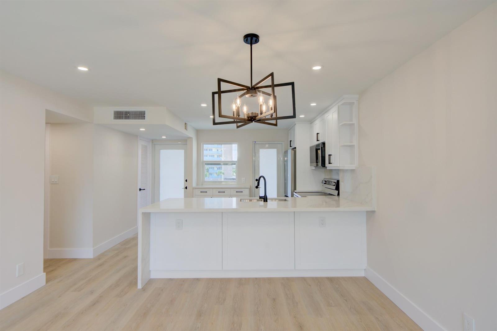 A modern kitchen features white cabinetry, a waterfall island, and a geometric chandelier — 201 N Ocean Boulevard # 207, Pompano Beach FL 33062, POMPANO BEACH, FL